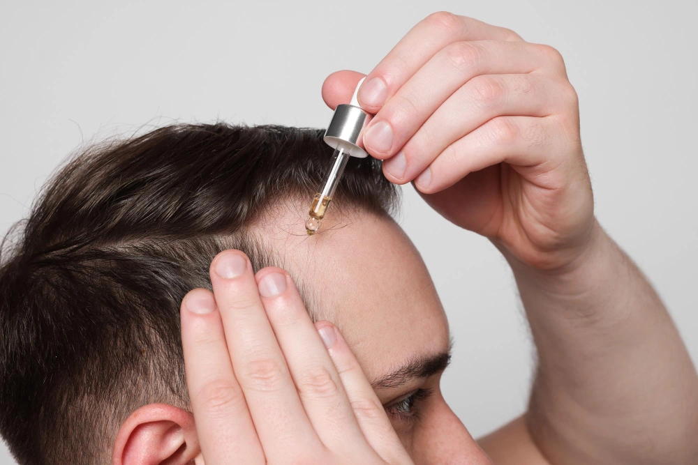 Homme appliquant un sérum capillaire sur un fond gris